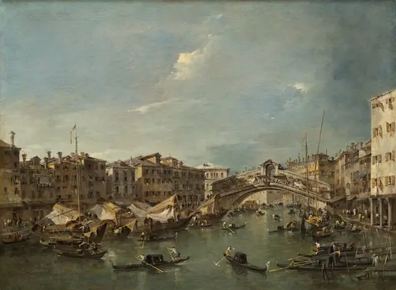 We look down and across a canal filled with more than two dozen gondolas and sailing boats, and flanked by rows golden-yellow and parchment-white buildings connected by a wide, arched bridge in this horizontal landscape painting.