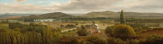 We look across the tops of trees down onto the roofs of a cluster of buildings and then a grassy expanse, a body of water, and rolling hills in this notably wide landscape painting. The trees are painted with shades of pine and olive green.