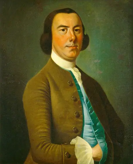 The image shows an upper-body portrait of a man facing forward with his body tilted slightly to the left. He wears a brown coat over a teal waistcoat and a white ruffled shirt is visible at the cuffs and neckline.
