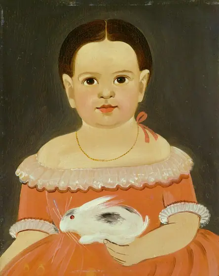 The image is a portrait of a young child shown from the waist up. The child is seated and facing forward. The child has dark hair that is styled smoothly and parted down the middle.