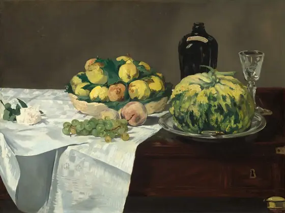 A white rose, grapes and other fruit, a squat gourd, a bottle, and a glass are arranged across a dark wood table partly covered by a white cloth in this horizontal still life painting.