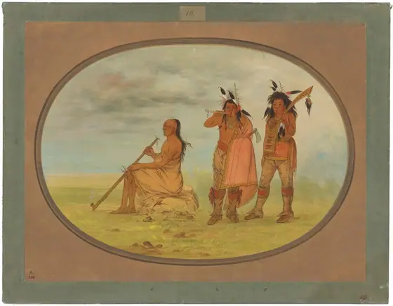 The image shows three individuals against a natural background. On the left, a man is seated on the ground, his body wrapped in a beige cloth. He has long, dark hair and a solemn expression, holding a long pipe.