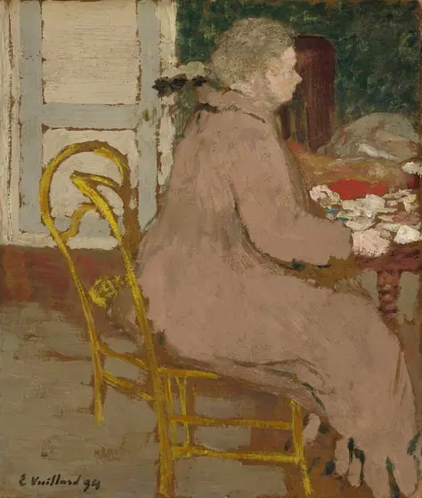 This painting shows a person seated at a table in a bright yellow chair, facing the right. The person has pale skin and gray hair, and they are wearing a loose-fitting light brown garment, similar to a long coat or dress.