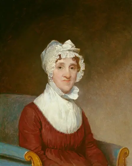 This painting shows the upper body of a woman seated in a chair. She is wearing a white bonnet with ruffled edges, covering her wavy, light brown hair. Her facial features include fair skin, thin lips, a long nose, and a pointed chin.