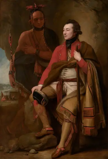 A man with pale white skin sits and a man with light brown skin stands in front of a cave-like, rocky outcropping in this vertical portrait painting.