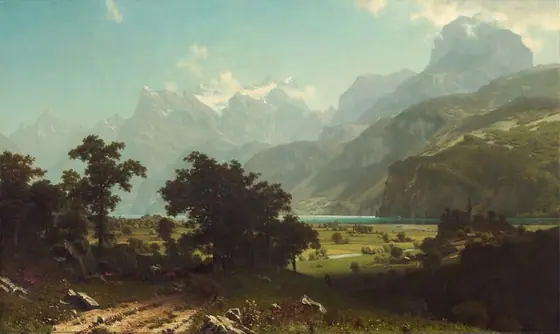 From a little above a dirt road, we look past a grove of trees to a broad plain and a lake at the foot of towering, hazy mountains in this horizontal landscape painting.